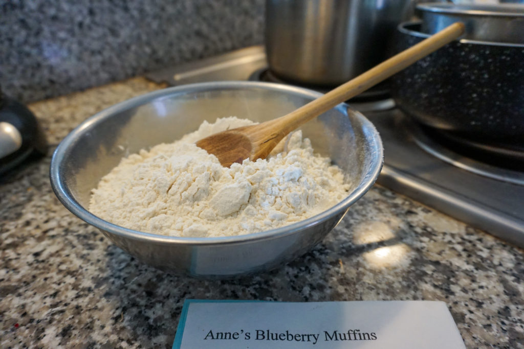 Bowl of Flour with recipe book of Anne's Blueberry Muffins with flour and a wooden spoon